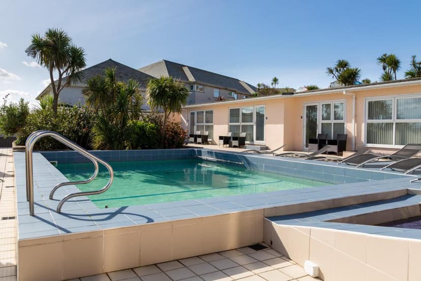 Outdoor swimming pool with palm trees and low-rise accommodation buildings under blue sky in Newquay.