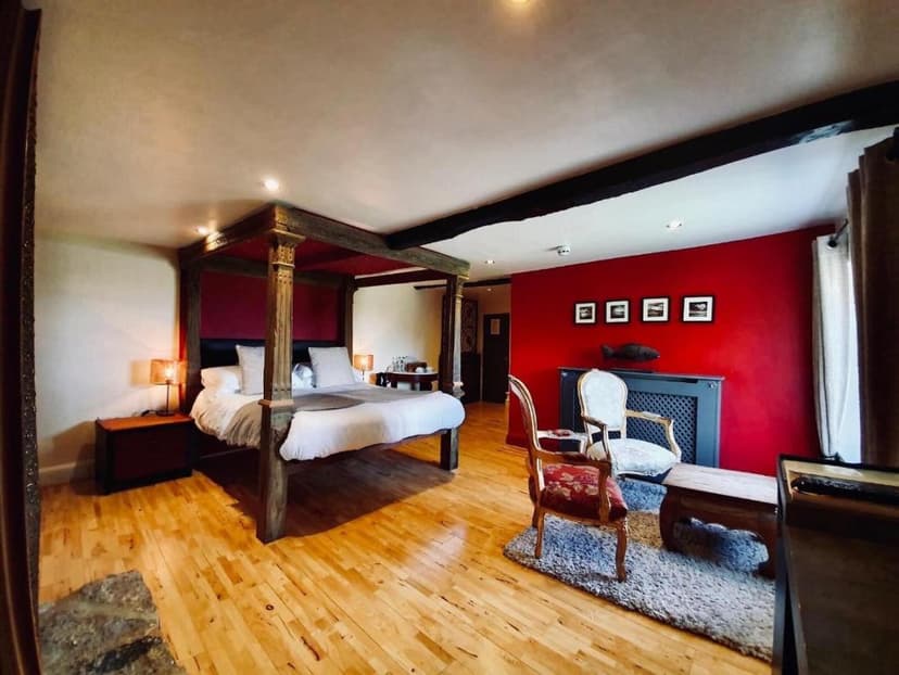 Bedroom with four-poster bed, wood floors, and a bright red accent wall with framed art.