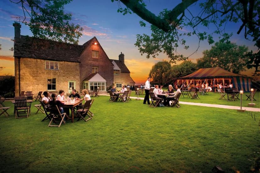 Outdoor dining on lawn beside stone building with large striped event tent at sunset