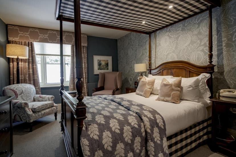 Four-poster bed with patterned bedding in a hotel room with floral wallpaper