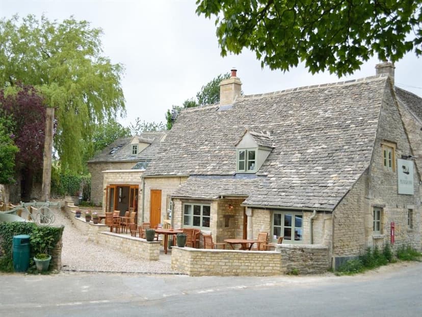 Stone pub with slate roof and outdoor seating next to a road with greenery