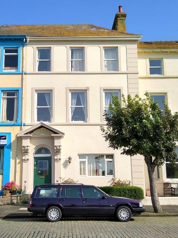 Terraced house with number 6, green door, and parked dark station wagon on cobblestones.