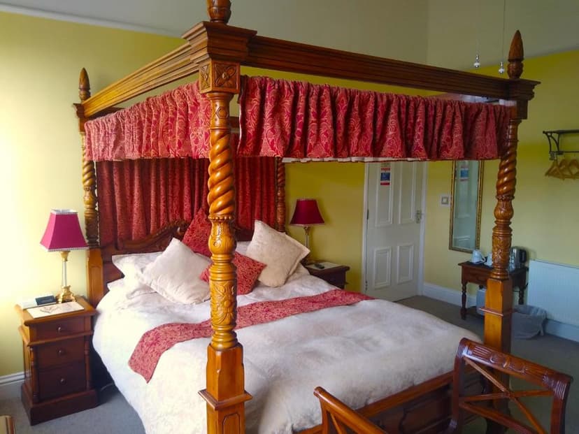 Four-poster wooden bed with red draped canopy and white bedding in a yellow room.