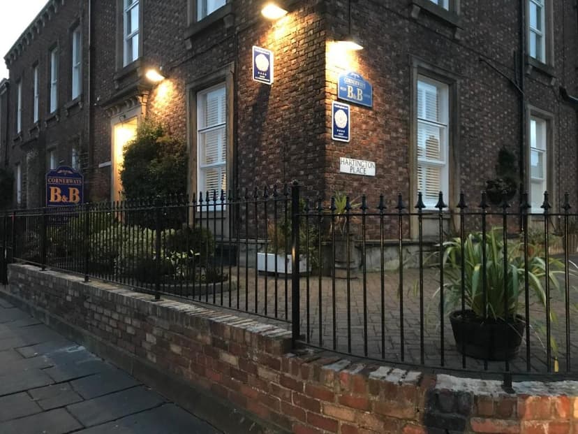 Cornerways B&B sign on brick building facade with black iron fence and potted plants