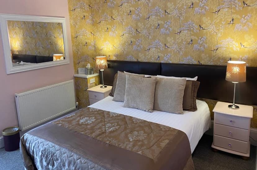Bedroom with bed, yellow bird wallpaper, bedside lamps, and white radiator