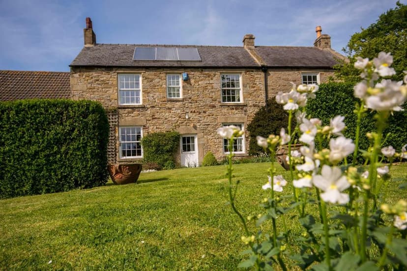 Stone farmhouse with solar panels, green lawn, and white flowers in the foreground.