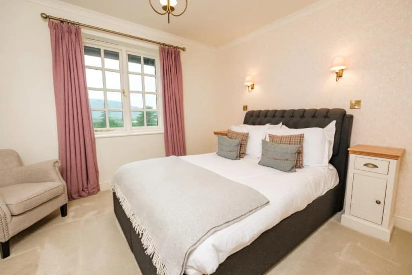Bedroom with tufted headboard, pink curtains, and view of green hills outside window.