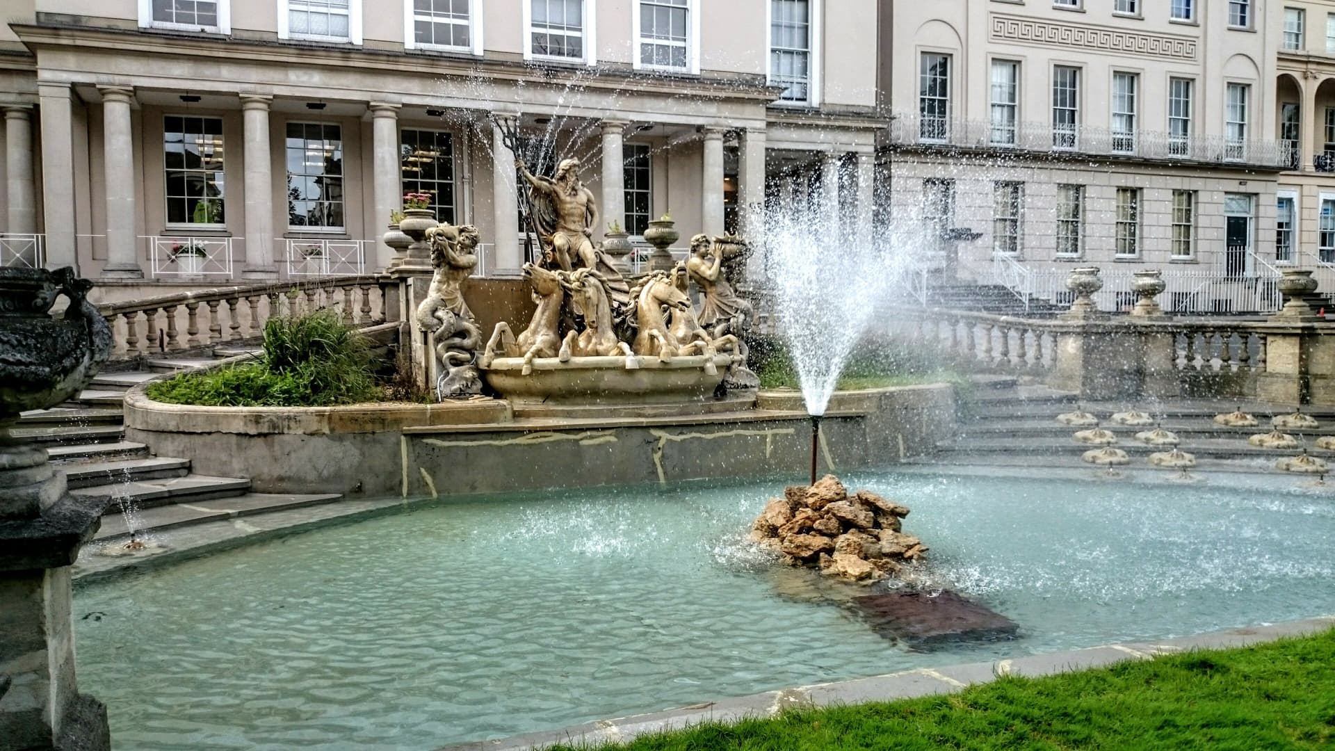 Neptune fountain with statues of horses and sea creatures in front of a classical building.