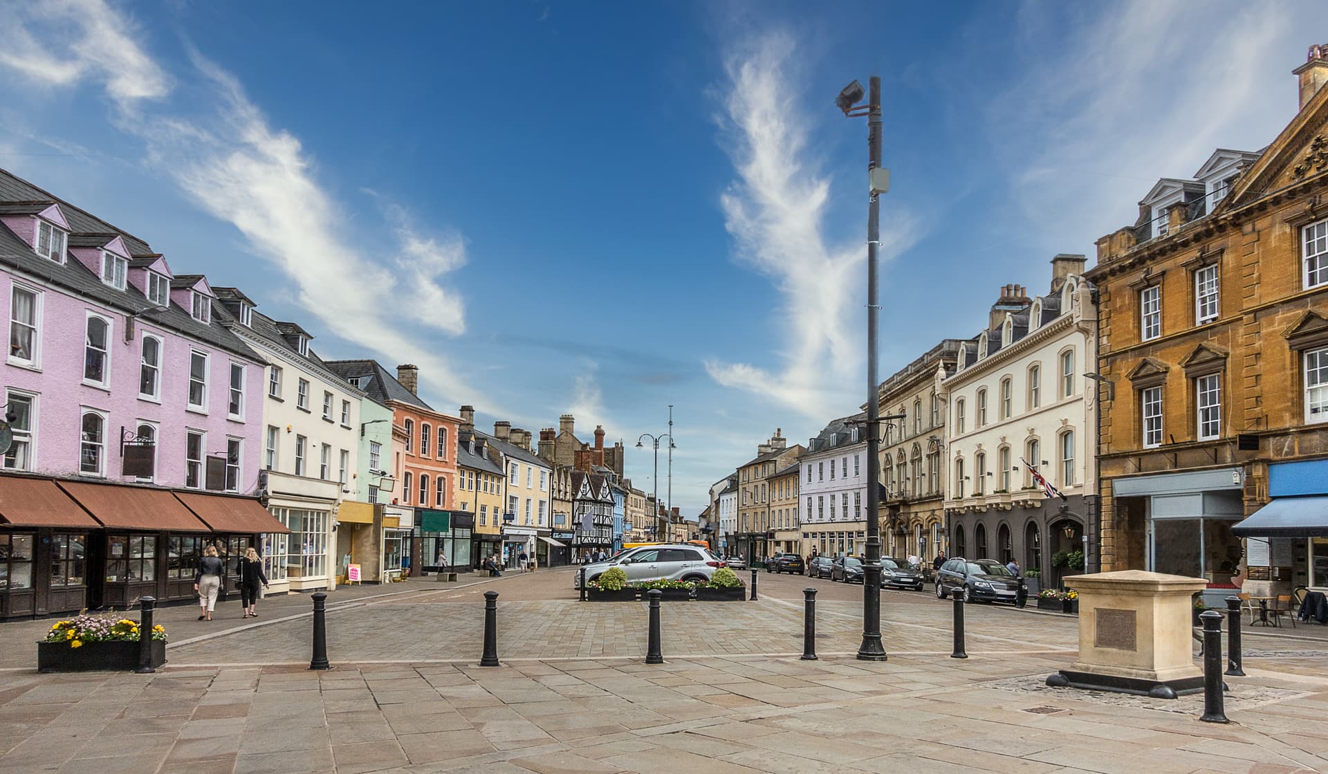 Historic town square with colorful shopfronts and blue sky in Cirencester