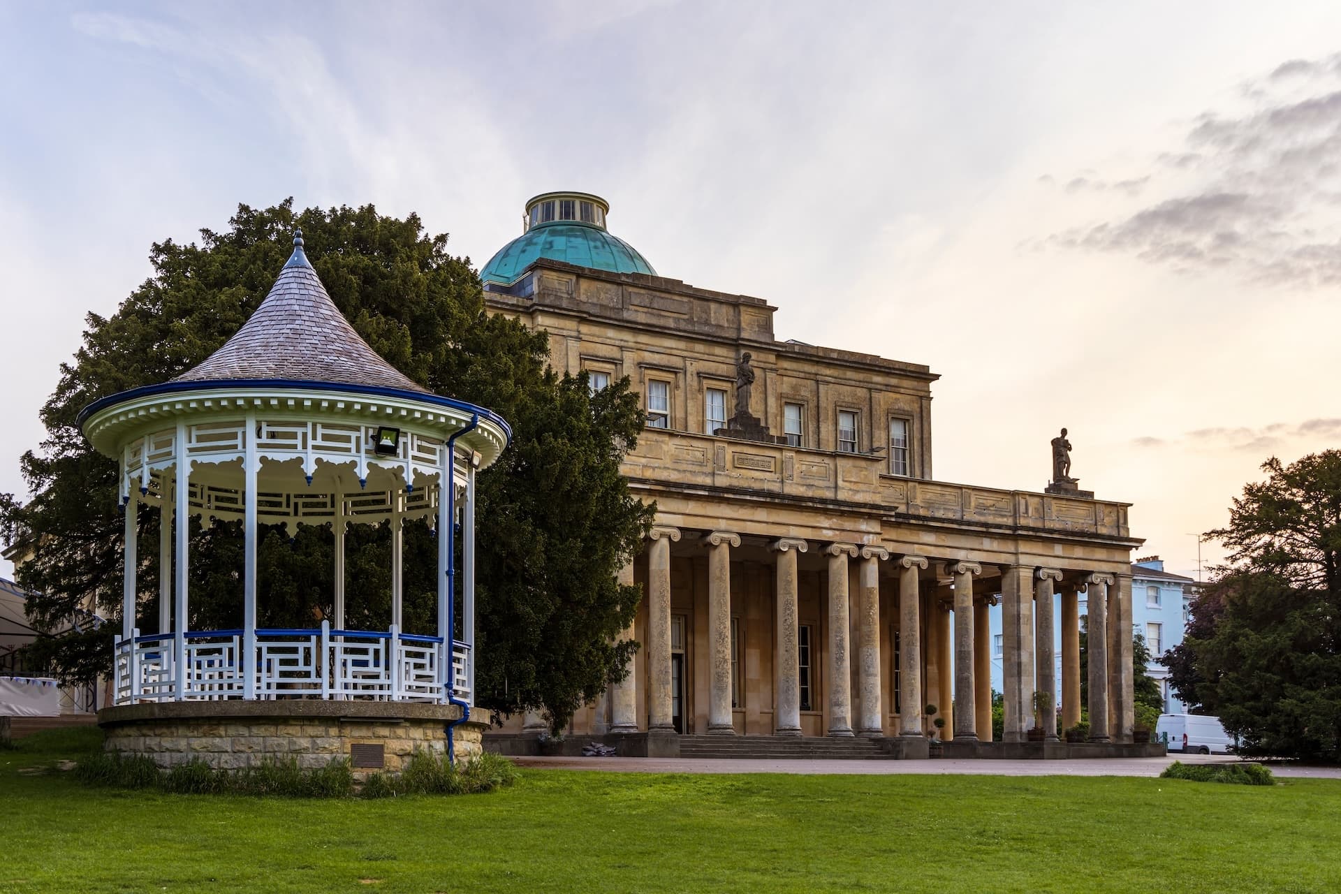 White wooden bandstand and neoclassical building with a green dome in Cheltenham park.