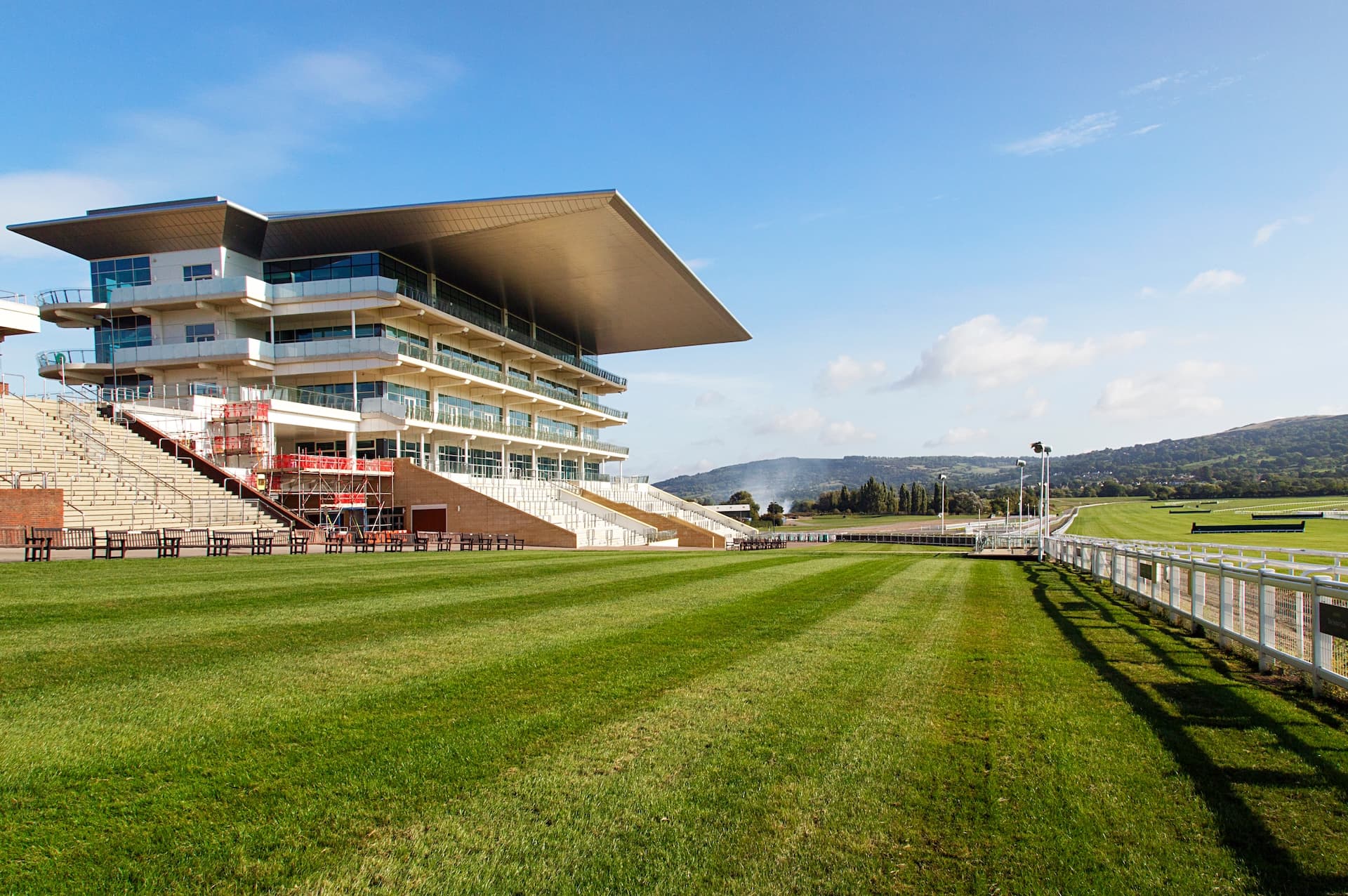 Modern grandstand next to green racetrack with hills in background at Cheltenham Racecourse.