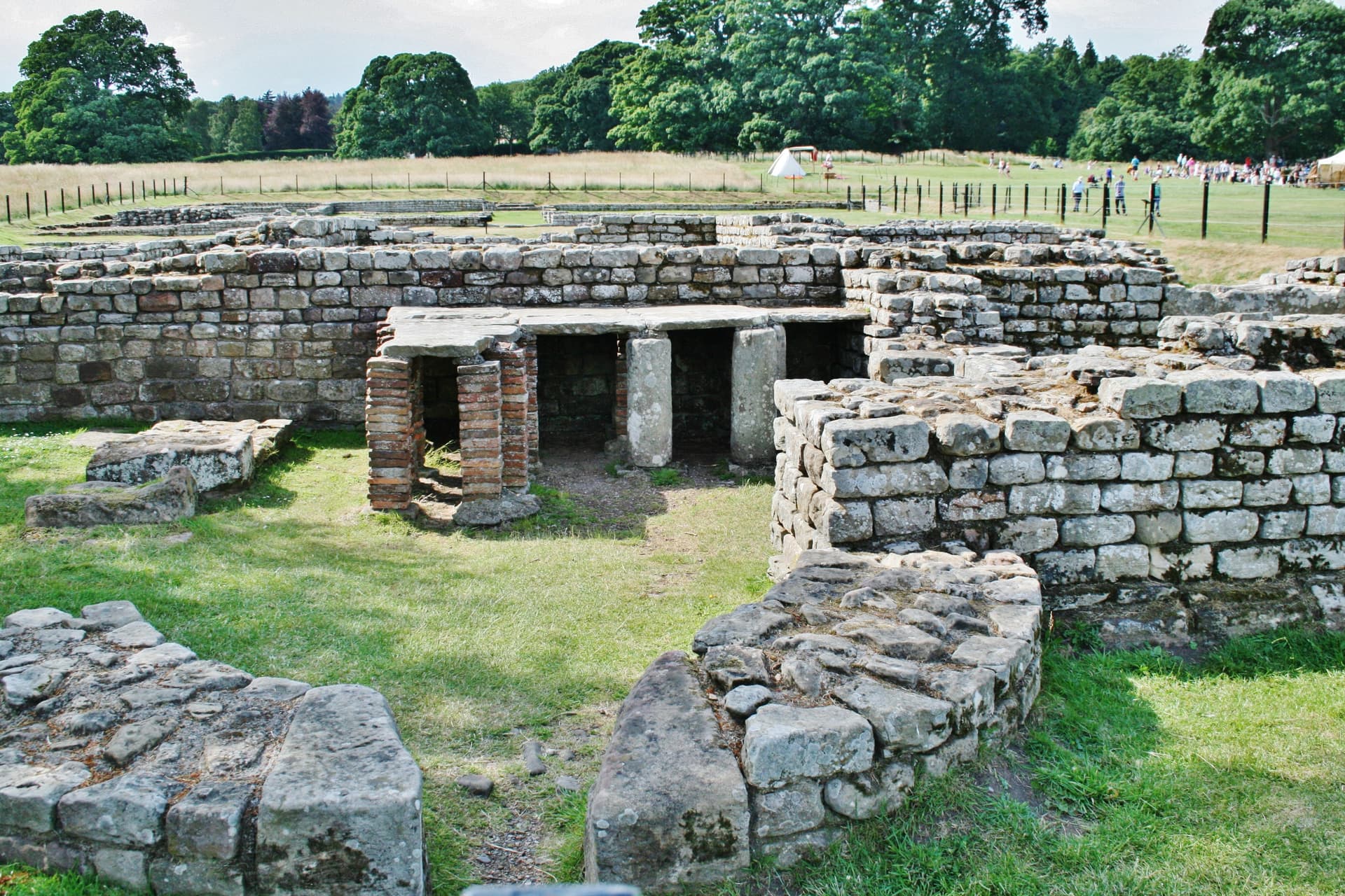Ruins of a stone Roman fort with brick hypocaust pillars in a grassy field.