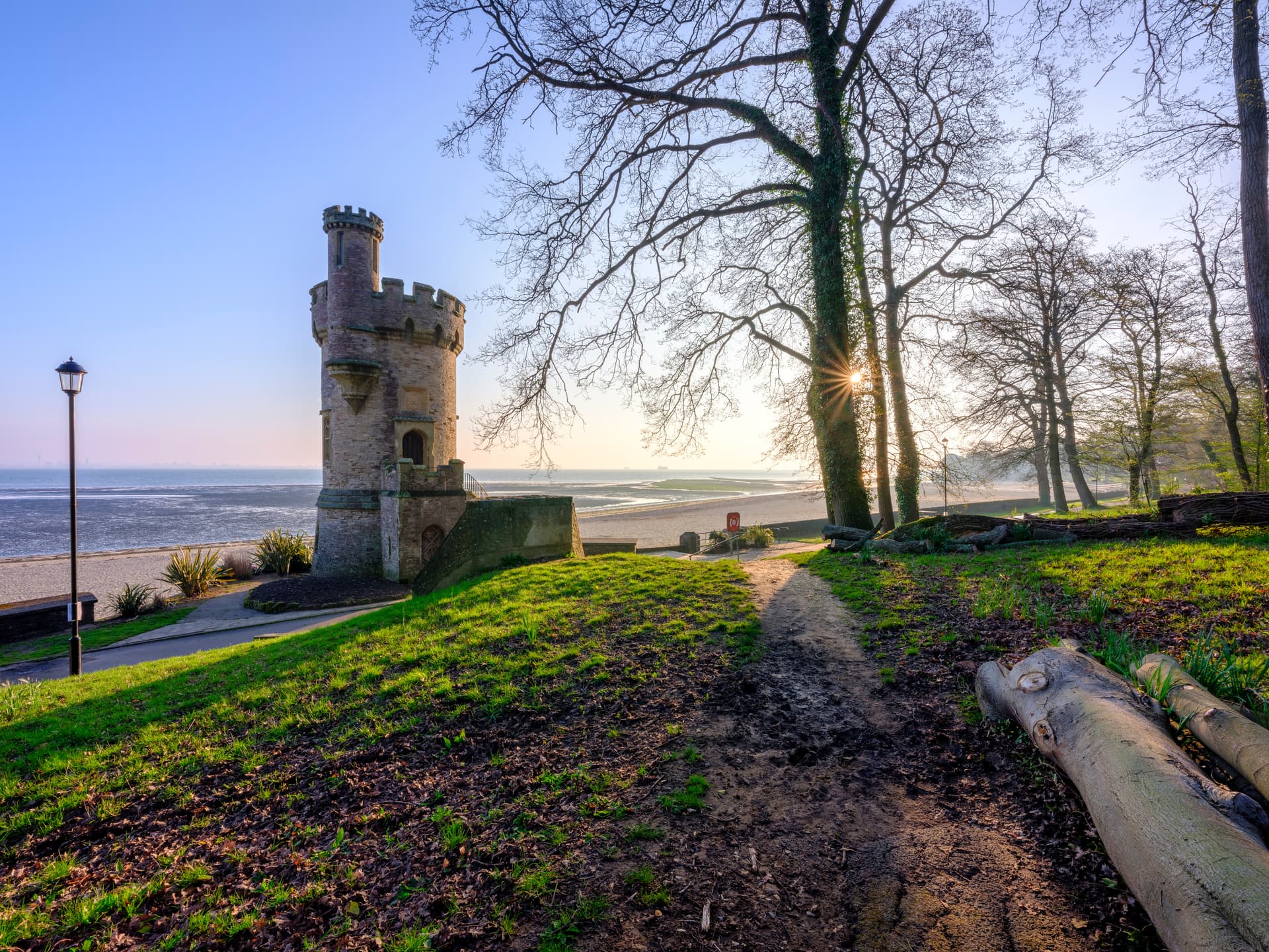 Stone tower by beach at low tide with sun setting through bare tree branches