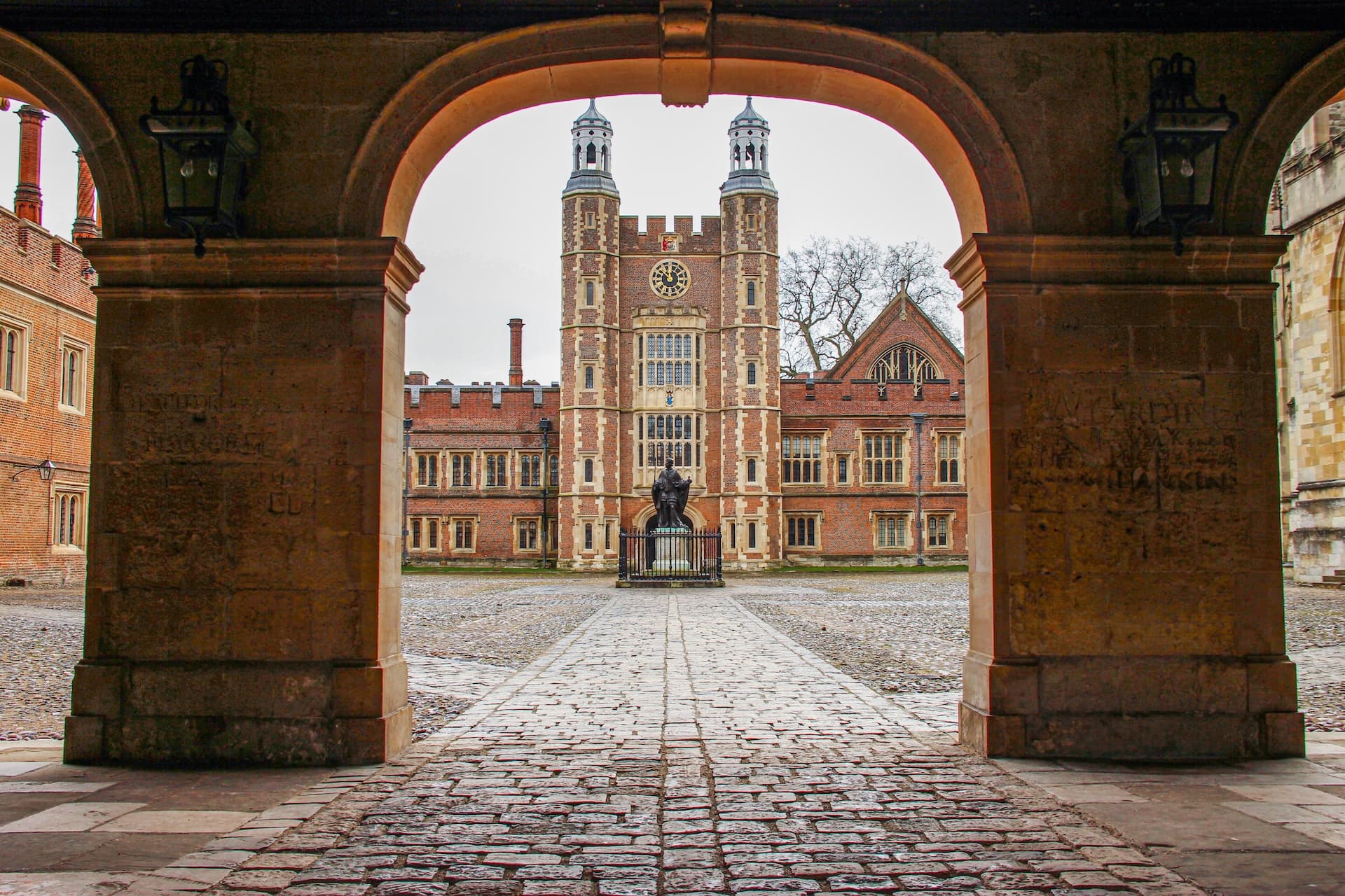 Tudor-style brick building with twin towers viewed through a stone archway at Eton College.