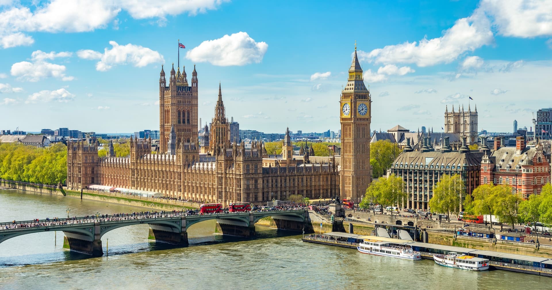 Palace of Westminster and Big Ben tower over the River Thames with bridge traffic in London.