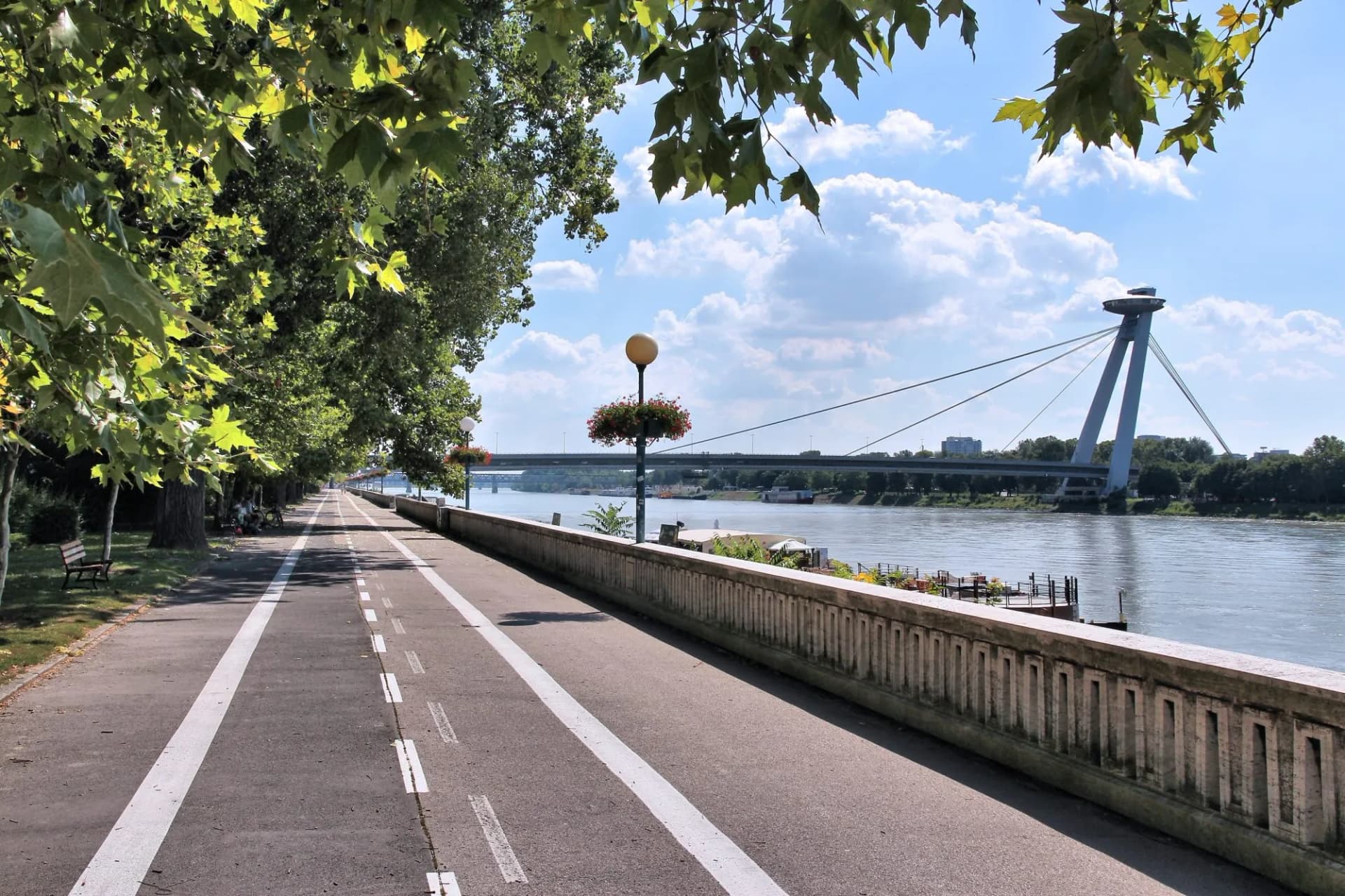 Cycling path along river next to bridge with UFO-shaped tower in Bratislava