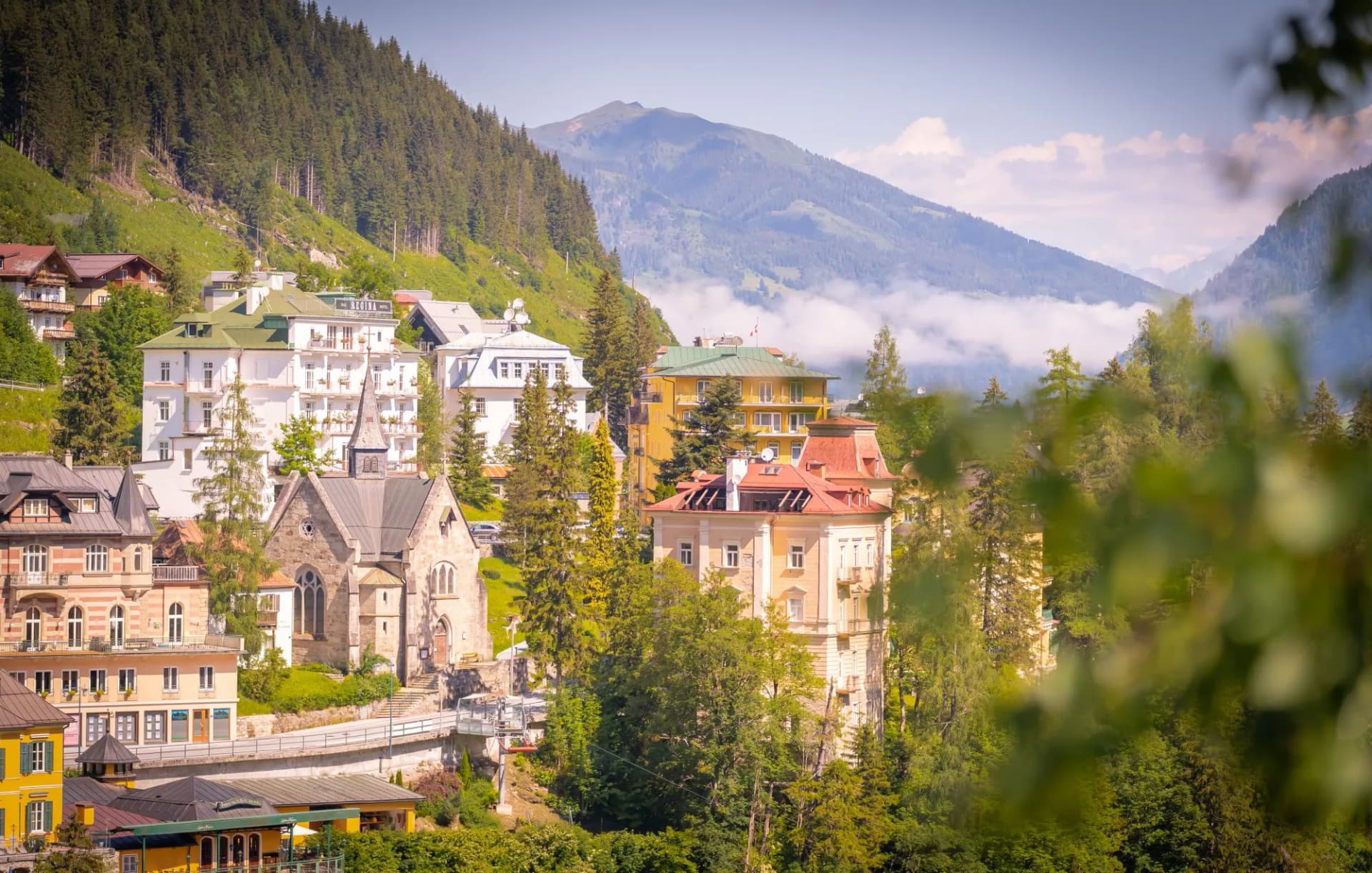 Alpine village buildings nestled on a steep, forested slope with mountains in the background in Bad Gastein.