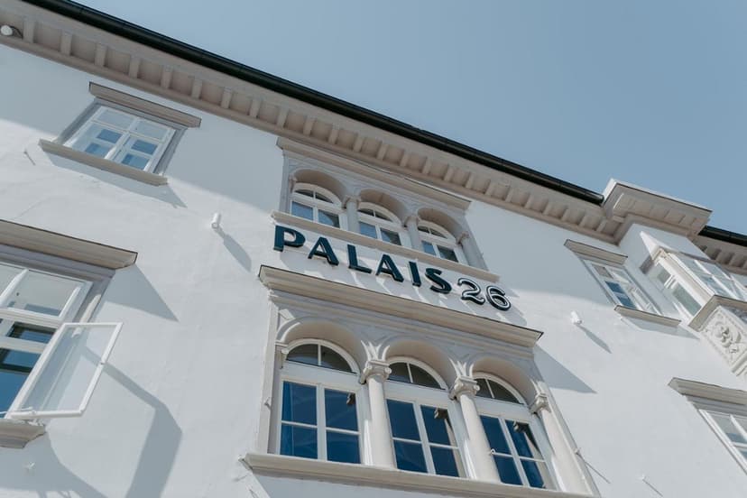 White historic building facade with "PALAIS 26" signage and arched windows under a clear blue sky.