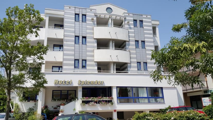 Hotel Splendor building facade with gray paneling, white balconies, and green trees against blue sky.