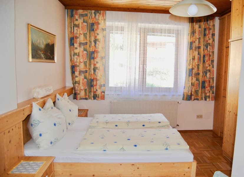 Twin beds with light blue floral bedding in a room with wood paneling and bright window.