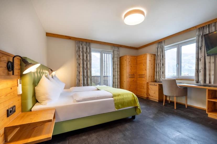 Hotel Hubertus room with green bed, wooden furniture, and mountain view from window.