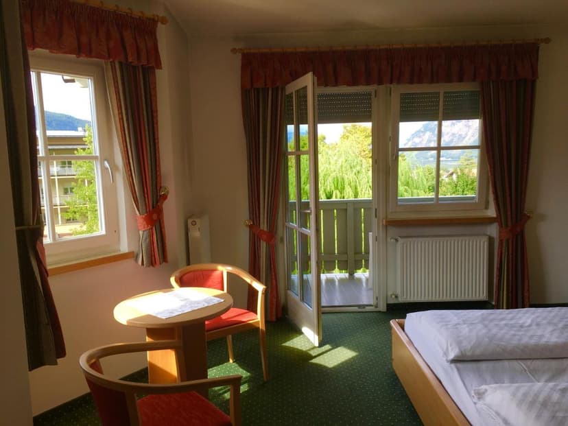 Hotel room with twin beds, small table, and balcony view of mountains and lake