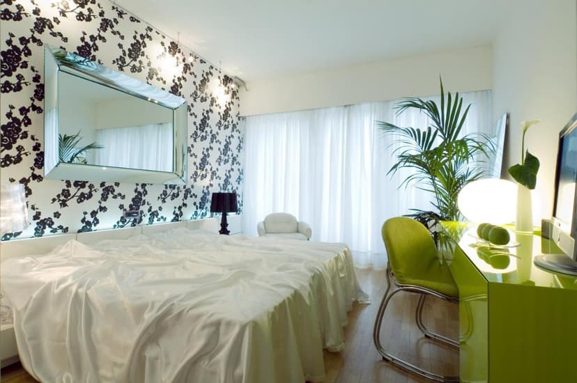 Modern hotel room with white satin bedding, black floral wallpaper, and a bright green desk area.
