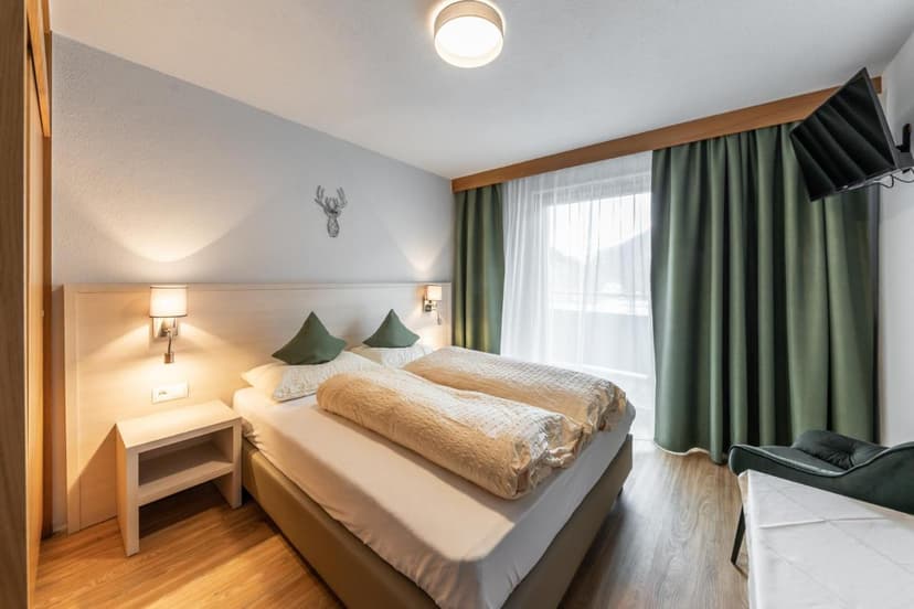 Bedroom with double bed, green accents, wood floor, and deer head wall art, Pension St. Lukas.