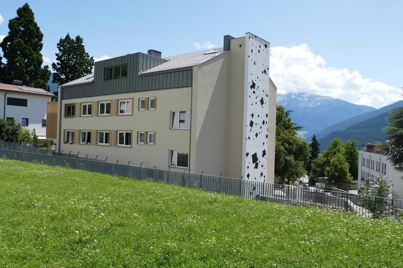 Modern apartment building with artistic facade detail overlooking green hillside and snowy mountains.