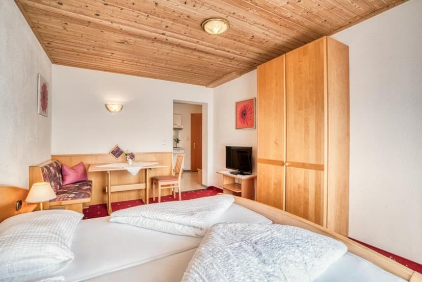 Bedroom with wooden ceiling, white bedding, light wood wardrobe, and small dining nook.