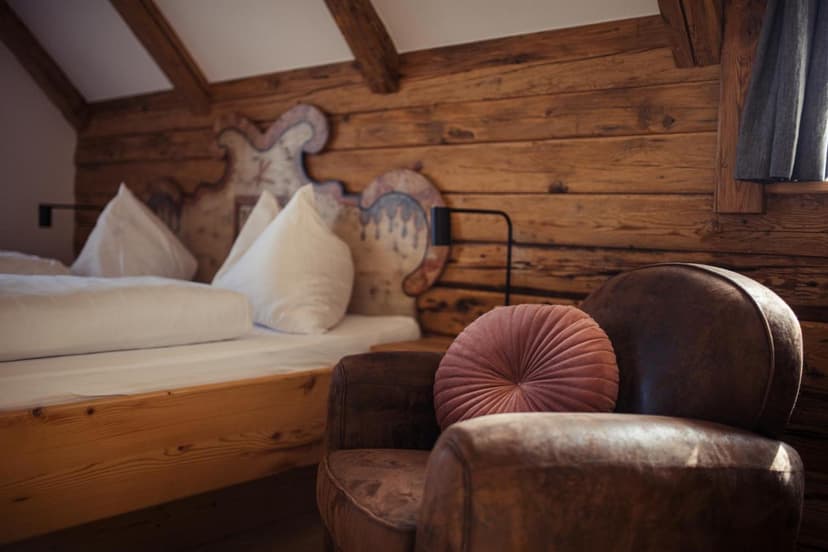 Cozy bedroom with wooden walls, white bedding, and a brown leather armchair with a pink cushion.