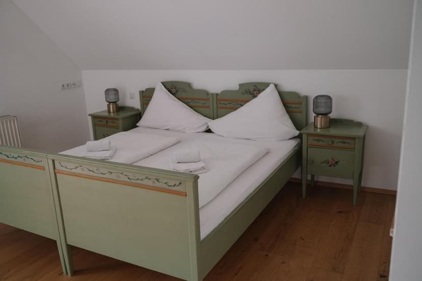 Double bed with painted green wooden frame and white linens in room at Pension Obertrum am See.