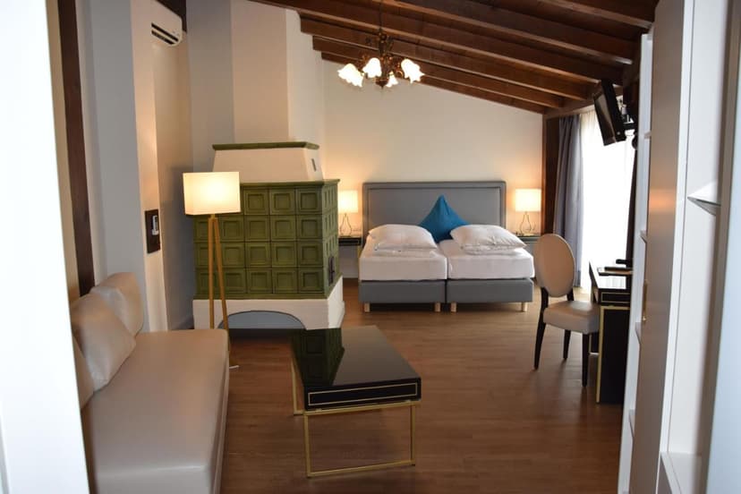Hotel room with twin beds, green tiled stove, and exposed wooden ceiling beams, Atel Hotel Lasserhof.