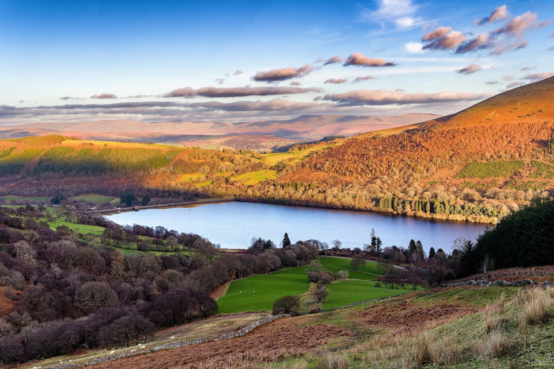 Reservoir in Brecon Beacons National Park with autumn foliage and rolling hills under blue sky.