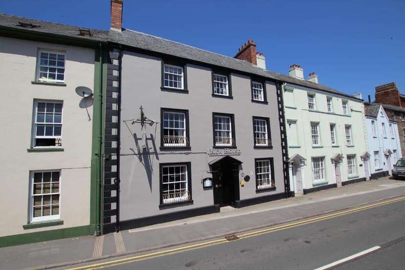 The Beacons Guest House, a gray building with white-paned windows, on a sunny street.