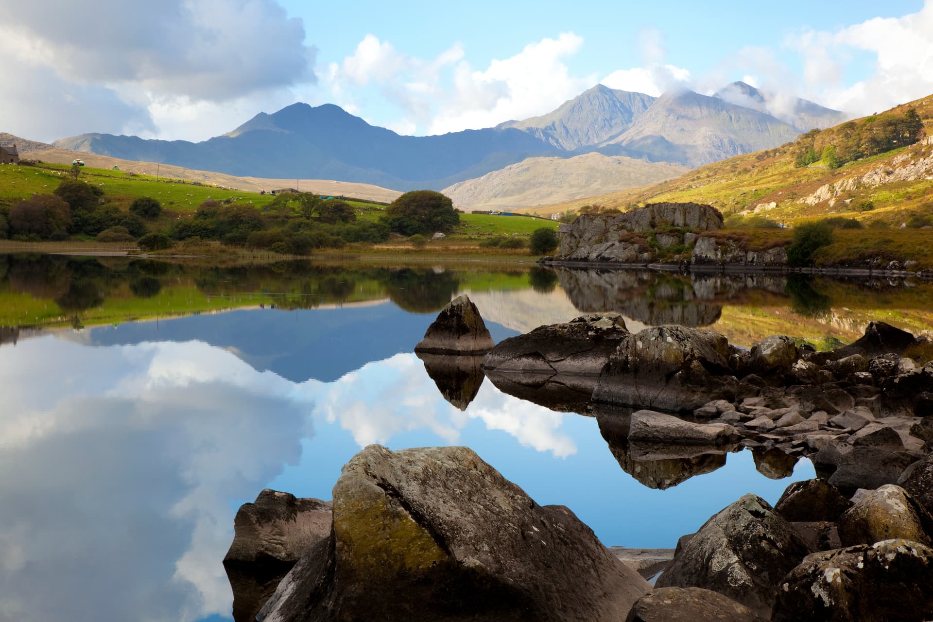 Mountain reflection in still lake water with foreground rocks, likely in the Cambrian Mountains.