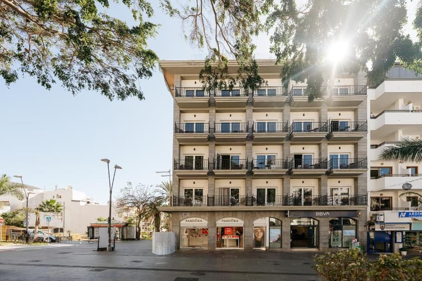 Hotel Reveron Plaza building with balconies on a sunny paved square with trees