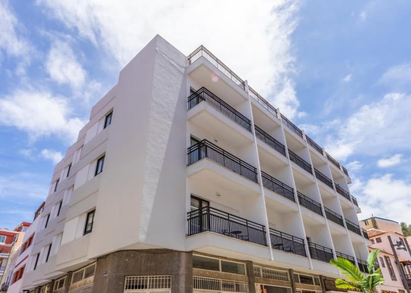 White multi-story building with black balconies against a bright blue sky with clouds