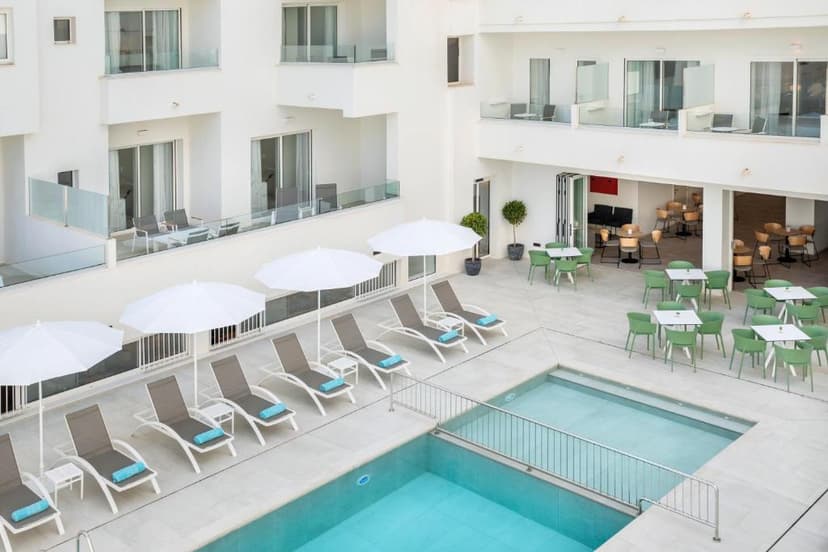 Aparthotel courtyard with swimming pool, sun loungers, white umbrellas, and outdoor dining area.