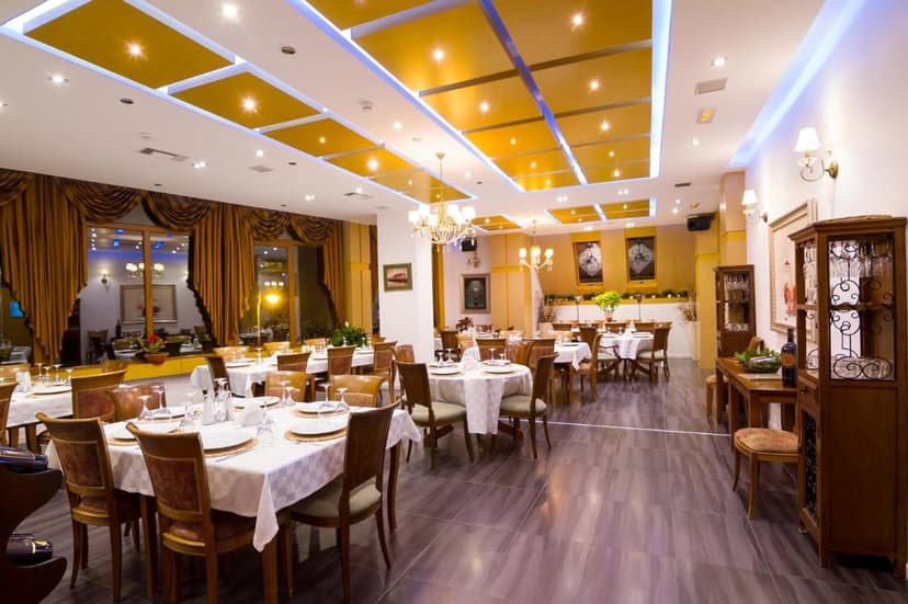 Restaurant dining room set with white tablecloths, warm lighting, and yellow ceiling panels.