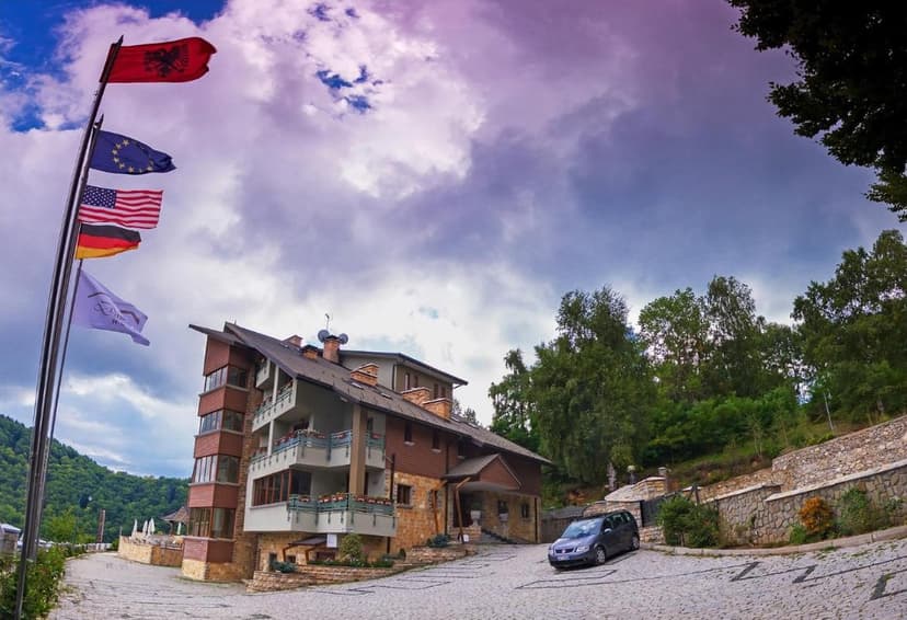 Hotel Dardha with Albanian, EU, US, and German flags flying under a dramatic sky.