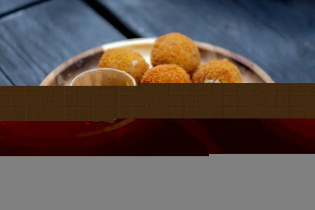 Fried bitterballen served with dipping sauce on a wooden plate on a dark surface