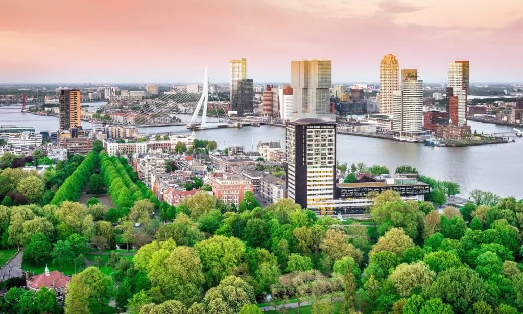 Skyline of Rotterdam with skyscrapers, river, and green park foreground at sunset