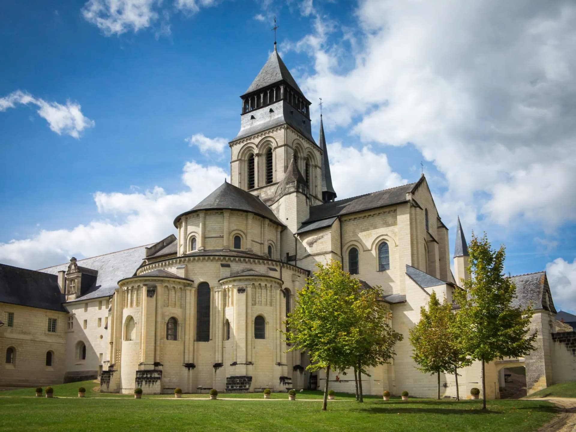 Romanesque abbey church with a central tower, green lawn, and blue sky with clouds.