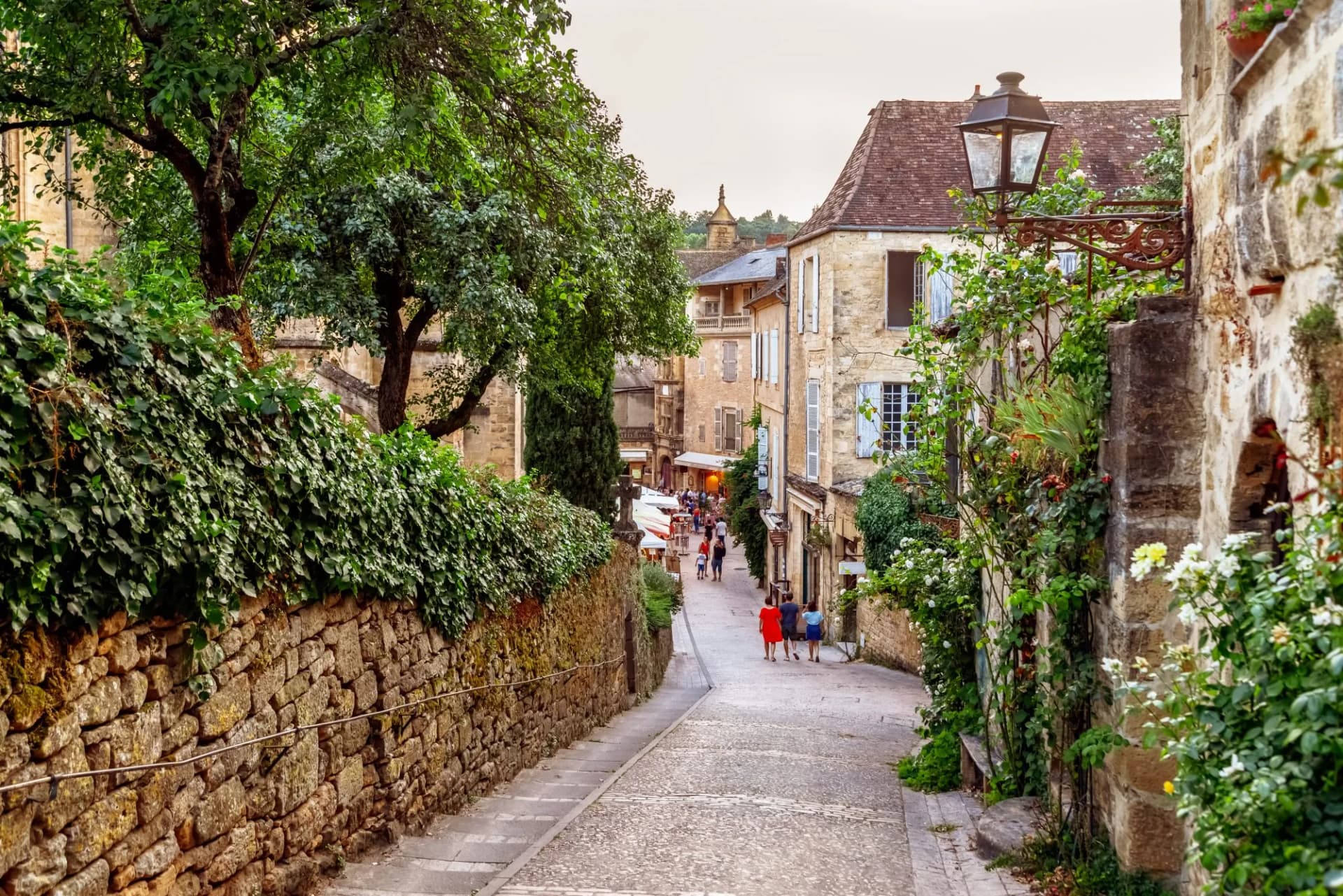 Cobblestone alley in Sarlat with stone walls covered in ivy and flowering plants.