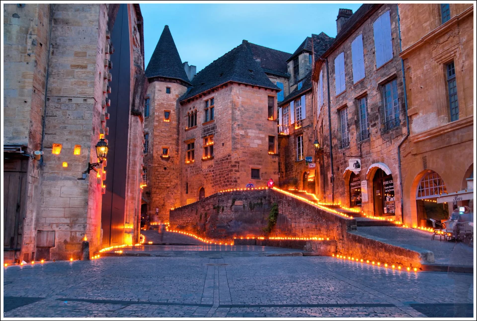 Cobblestone street in Sarlat old town illuminated by many small lights at dusk.