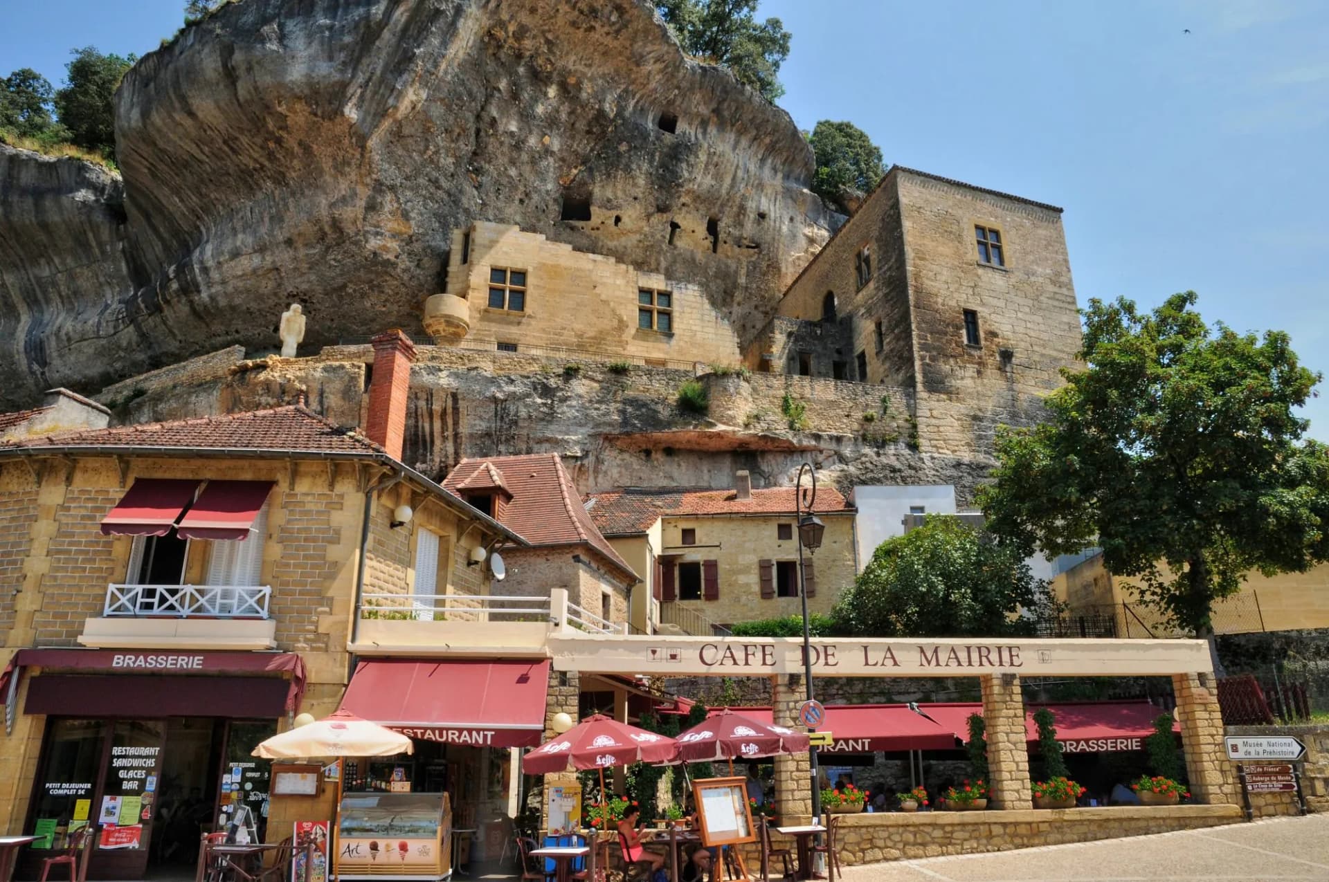 Cafe de la Mairie and brasserie below cliffside buildings in Les Eyzies tourist village.