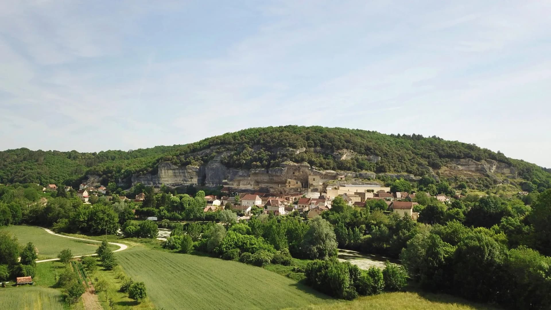 Village nestled at the base of a forested cliff face with troglodyte dwellings in Les Eyzies.