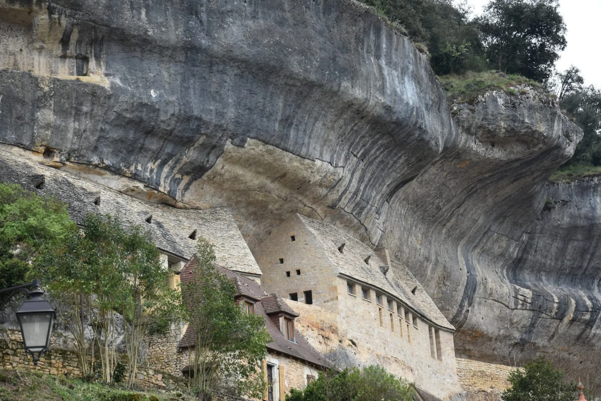 Stone houses built into a massive cliff overhang in Les Eyzies, France.