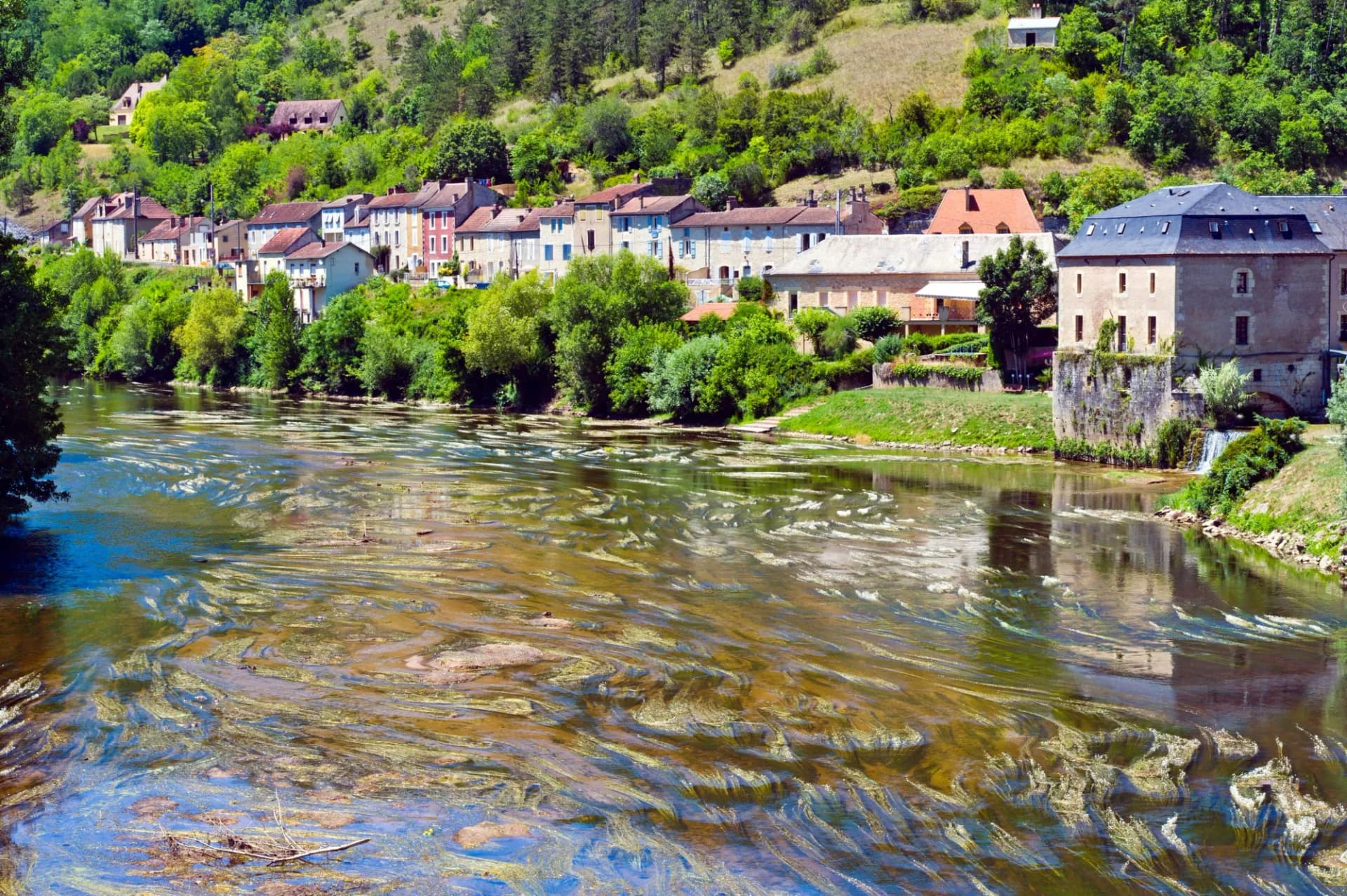 River flowing past historic stone buildings nestled in green hills of Vezere towns.